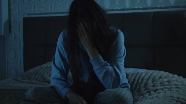 Genç bir kadın gece yatağında şaşkın ve dikkatsiz bir şekilde oturuyor. Sisli zihni ve duygusal yorgunluğu uykusuzluğu, iç mücadeleyi ve zihinsel dengesizliği yansıtıyor.. 