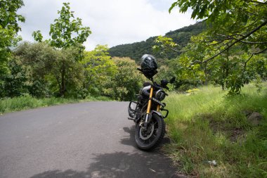 Gautala autramghat Sığınağı, Maharashtra, Hindistan-Ağustos 31, 2025: Yoğun yeşil bitki örtüsüyle çevrili manzaralı dalgalı bir tepe yolu boyunca parkedilmiş bir TV 'ler ronin' motosikleti