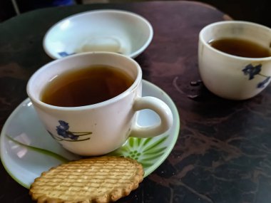 Süslü bir tabakta yanında bisküviyle servis edilen siyah çay fincanları.