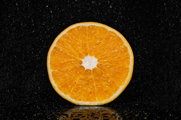 Juicy orange on a black background with splashing water. Natural product. Fresh citrus fruit