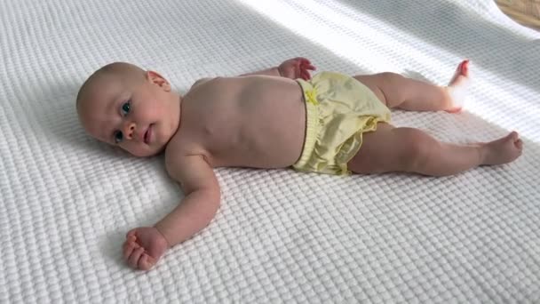 Bebé sonriente acostado en la manta blanca que mueve brazos y piernas — Vídeos de Stock