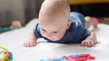 Bebek karnında yere uzanmış oyuncaklara gülümsüyor