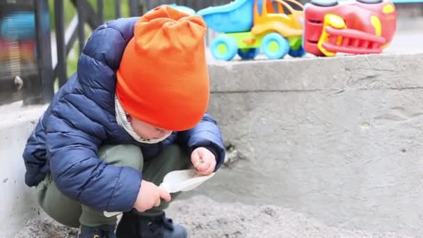 3-letni chłopiec bawi się i kładzie piasek w jego czerpaku na zewnątrz — Wideo stockowe