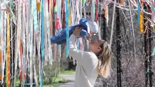 Matka drží své dítě nad hlavou d líbání ho venku v barevných stuhách — Stock video
