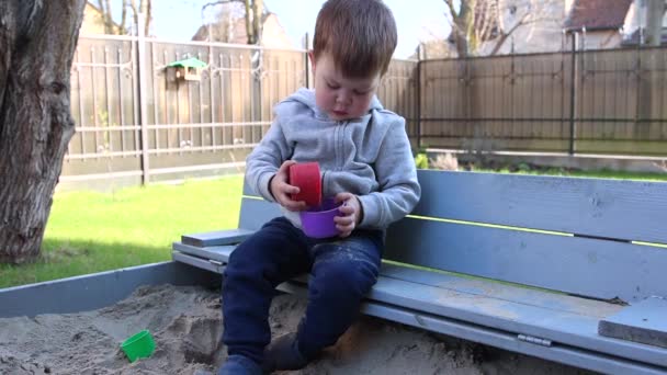 Mały chłopiec bawi się piaskiem w piaskownicy — Wideo stockowe