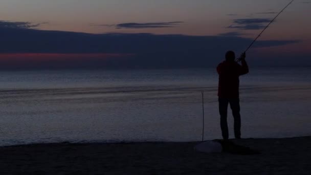 Sonnenuntergang Silhouette eines Fischers wirft Angelrute ins Meer — Stockvideo