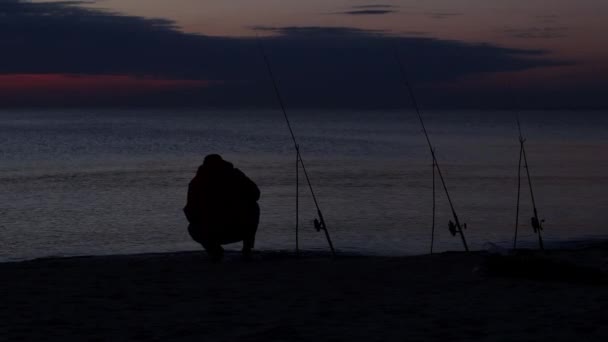 Silhouet van zittende visser aan de kust bij zonsondergang — Stockvideo