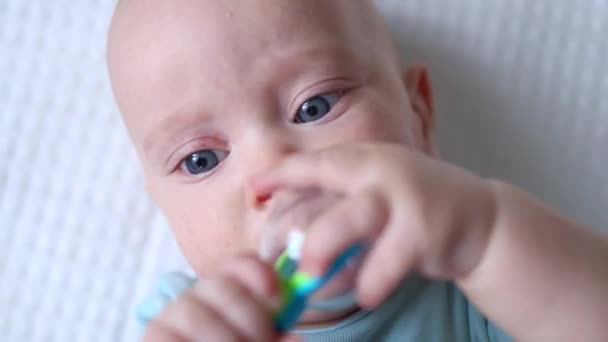 Portrait of blue eyed baby with toy in the mouth — стоковое видео