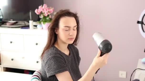 Молода брюнетка жінка сушить волосся вдома, сидячи на стільці — стокове відео