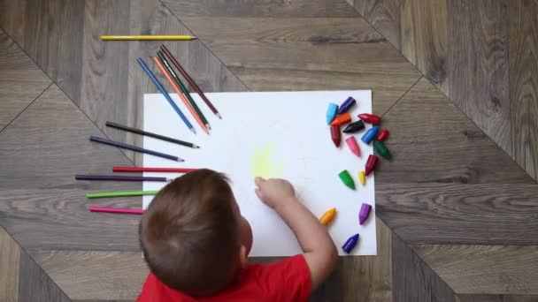 Niño pequeño dibujando sol con lápices acostados en el suelo en la sala de estar, vista superior — Vídeos de Stock