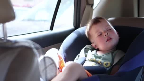 Niño pequeño durmiendo en un asiento de coche con sudor húmedo y mejillas rojas en clima caluroso — Vídeos de Stock