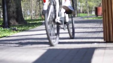 Bisiklet tekerlekleri ve pedal çeviren bacakların parkında bisiklet süren insanlar.
