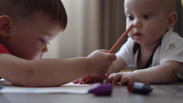 Dzieci interakcja mały chłopiec próbuje rysować podczas niemowlę chwyta jego ołówek — Wideo stockowe