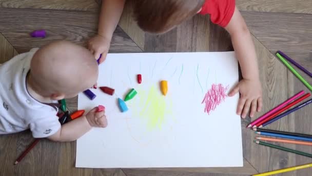 Kojenec ležící na podlaze a hrát si s pastelkami, zatímco malý chlapec kreslí — Stock video