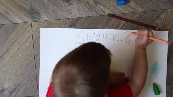 Little preschool boy lying on the floor and drawing summer picture with pencils, top view — Stock video