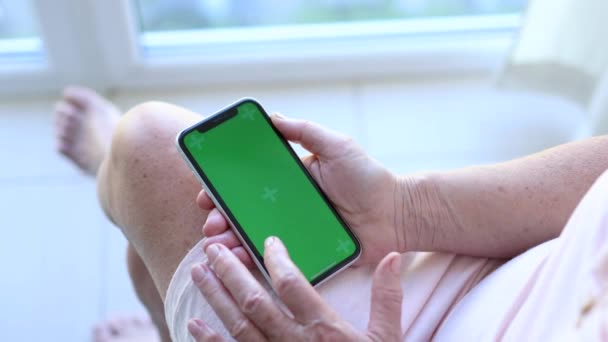 Пожилая женщина держит в руках смартфон с зеленым макетом экрана — стоковое видео