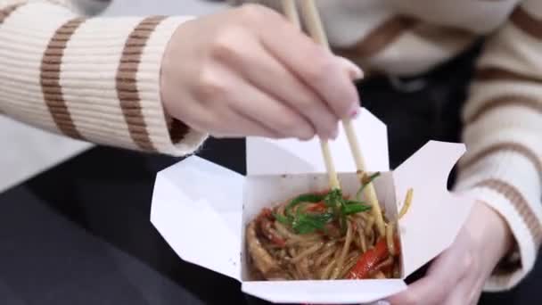 Женские руки перемешивают азиатскую лапшу с китайскими палочками в картонной коробке — стоковое видео
