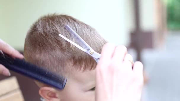 Porträtt av en pojke som klipper sig med sax och kam. närbild visa slow motion — Stockvideo