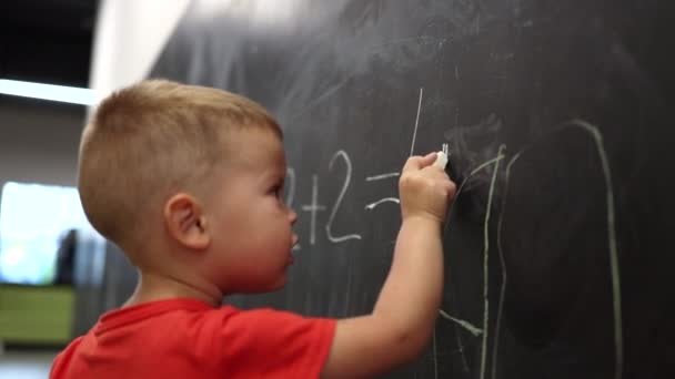 A piros inges kisfiú matekfigurákat ír táblára. — Stock videók