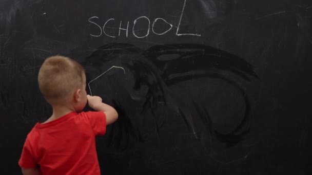 Liten pojke unge i röd skjorta drar sol på svarta tavlan med skolan skrifter på svarta tavlan — Stockvideo