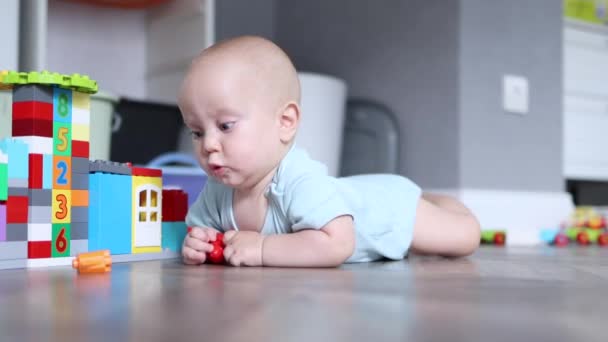 Pequeno bebê infantil de 6 meses tentando rastejar no chão de madeira brincando com brinquedos — Vídeo de Stock