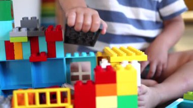 Küçük bebek eller plastik oyuncak tuğlalarla ve bina bloklarıyla oynuyor.