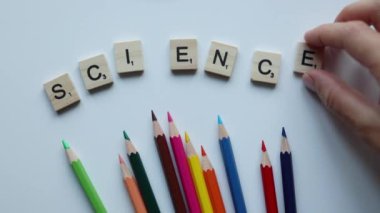 hand writing word science with wooden scrabble letters with colorful pencils on white background