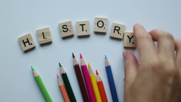 Hand componeren woord geschiedenis met houten letters en kleurrijke potloden op witte achtergrond. terug naar school concept — Stockvideo