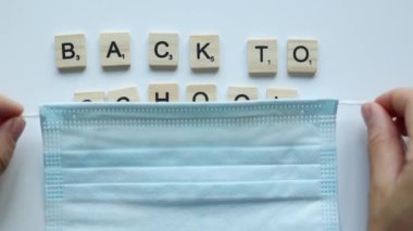 taking off facial mask from words back to school composed from wooden letters on white background. anti-covid concept