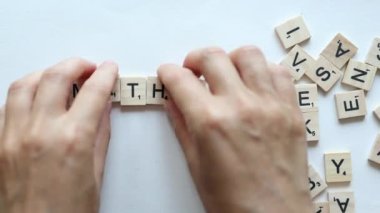 hands composing word maths from wooden letters on white background