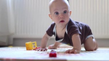 cute baby infant in brown clothes tries to crawl on the floor looking into the camera