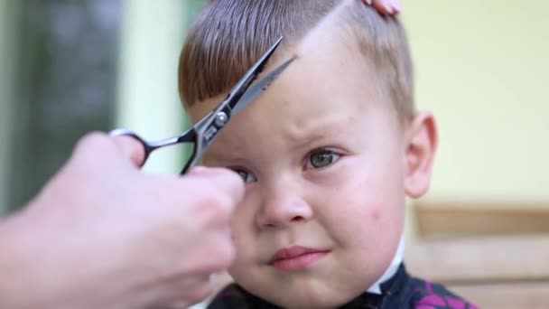 Känslor på små pojkar ansikte medan frisörer hand med sax skära håret på fransar smällar — Stockvideo