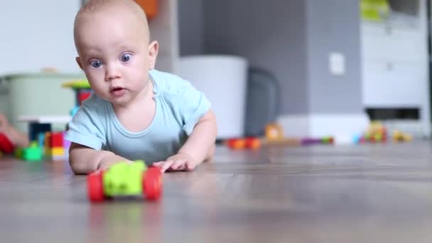 Pequeno bebê infantil de 6 meses tentando rastejar no chão de madeira brincando com brinquedos — Vídeo de Stock