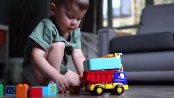Маленький мальчик играет с игрушками на полу дома — стоковое видео