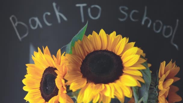 Terug naar school woorden op een zwart schoolbord en gele zonnebloemen voor de deur — Stockvideo