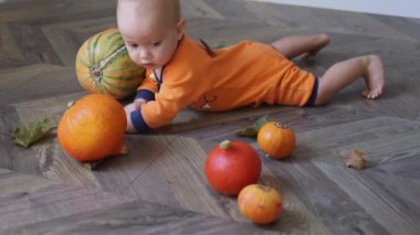 Turuncu kostümlü bebek balkabağı ve sonbahar kuru yapraklarıyla yerde yatıyor.