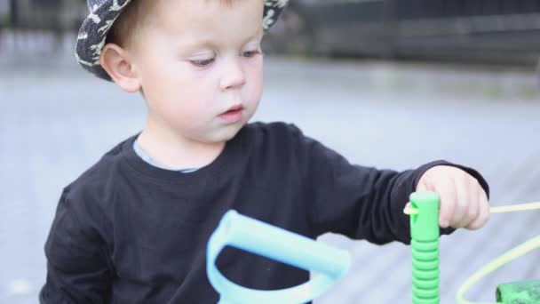 Caucasian child kid boy playing outside learn to thread rope string through hole — Stock Video