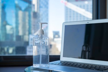 Ofisteki dizüstü bilgisayarın önünde el dezenfektanı duruyor. 