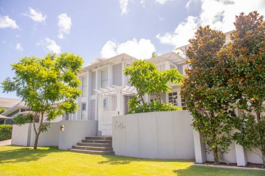 Güzel, lüks bir tatil köyü, yeşil ağaçlar ve bitkilerle dolu beyaz bir bina.