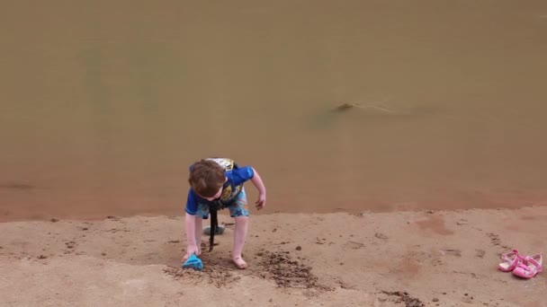 Pojke leker på stranden av floden — Stockvideo