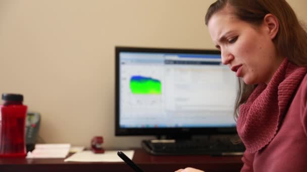 Frau schreibt SMS, während sie im Büro arbeitet — Stockvideo