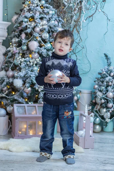 baby in a sweater with a Christmas tree toy and a Christmas tree