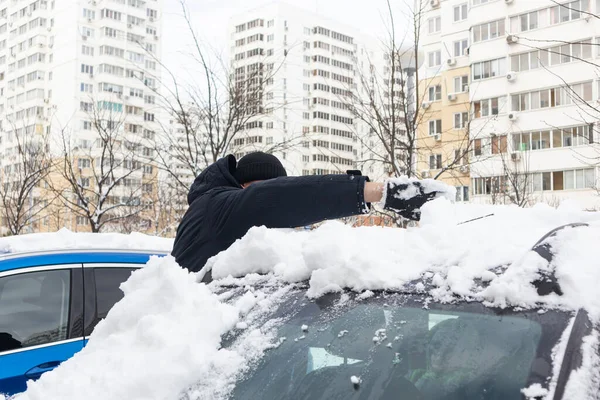 Adam arabayı kardan temizler.