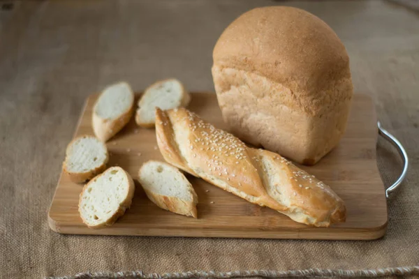 Pão inteiro fresco e fatiado em uma tábua de madeira — Fotografia de Stock