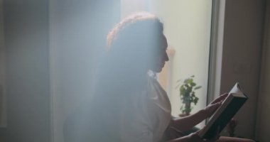 Kitap okuyan kadının üzerine güneş ışığı vuruyor.