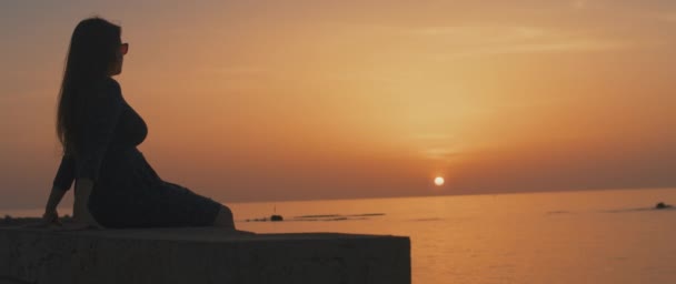 Mujer sentada en una pared de piedra al atardecer — Vídeos de Stock