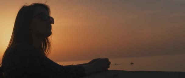 Kvinnan lutar sig mot stenmuren vid solnedgången — Stockvideo