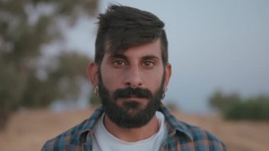 Sakallı adam kameraya bakıyor.