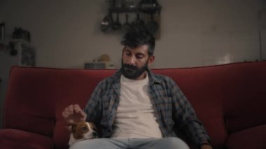 Adam kanepede oturup köpeğini okşuyor.