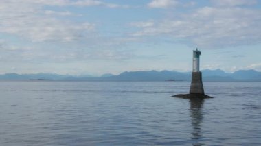 Pasifik adası koyunda arka planda karlı dağlar olan bir deniz feneri kulesi.. 